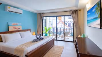 Habitación de hotel con cama, escritorio, balcón con sillas, planta en maceta y un cuadro de playa.