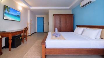 A hotel room with a bed, a desk, a chair, a TV, and an air conditioning unit.