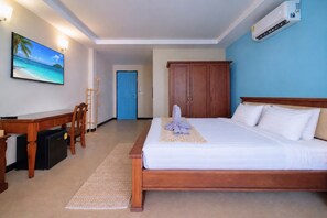 A hotel room with a bed, a desk, a chair, a TV, and an air conditioning unit.