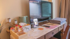 Habitación de hotel con escritorio, televisor de pantalla plana, espejo, ventana con vistas a un edificio y una cama.