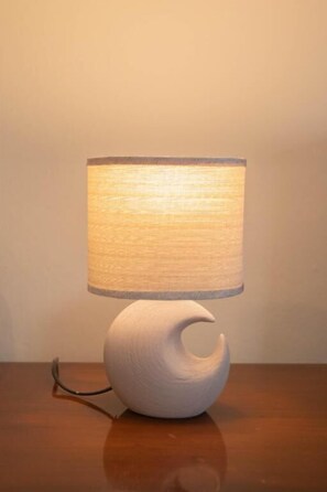 Une lampe de table blanche et moderne, dotée d’un abat-jour cylindrique, posée sur une table en bois.