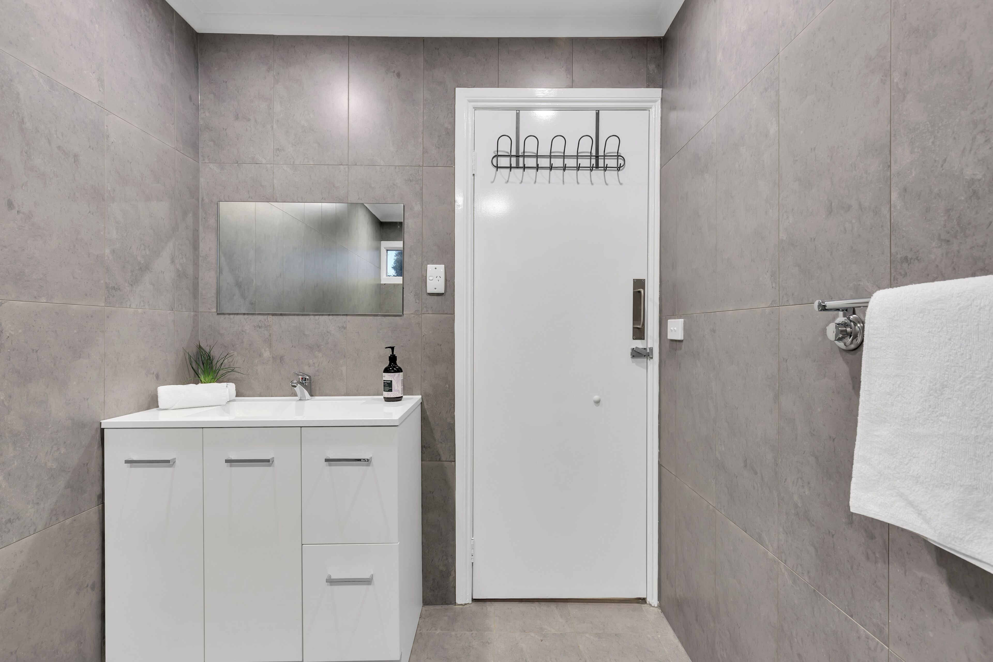 A modern bathroom with a white vanity, a large mirror, and a towel rack.