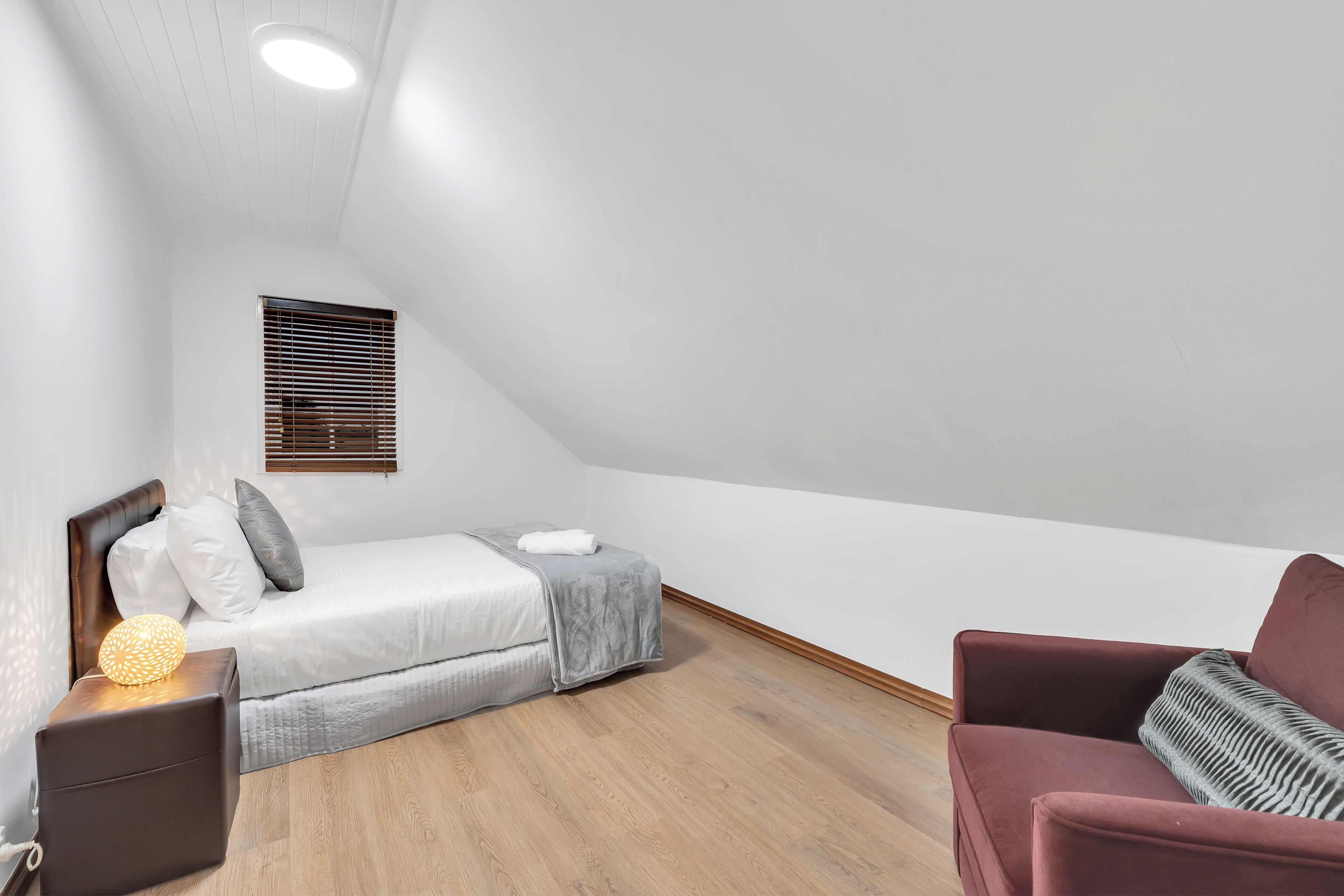 Une petite chambre à coucher moderne, avec un lit, une table de chevet, une chaise et une fenêtre équipée de stores.