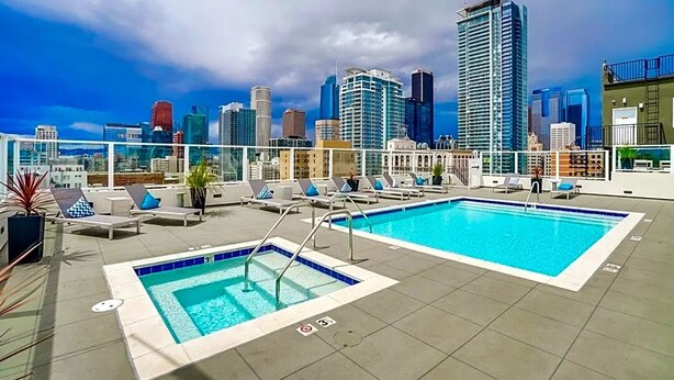 Una piscina sul tetto con lettini e uno skyline urbano sullo sfondo.