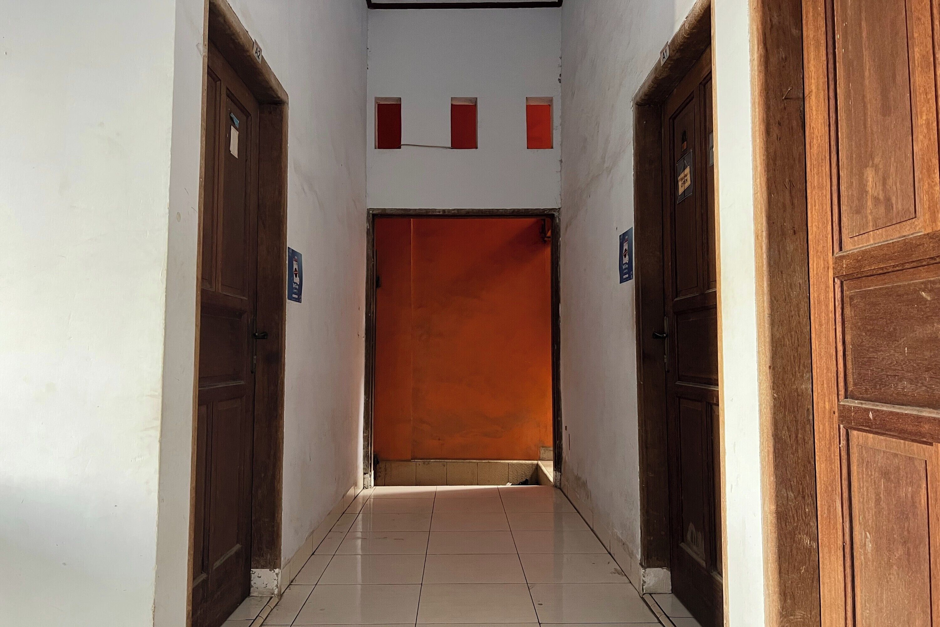 A narrow hallway with wooden doors on either side and a bright orange wall at the end.