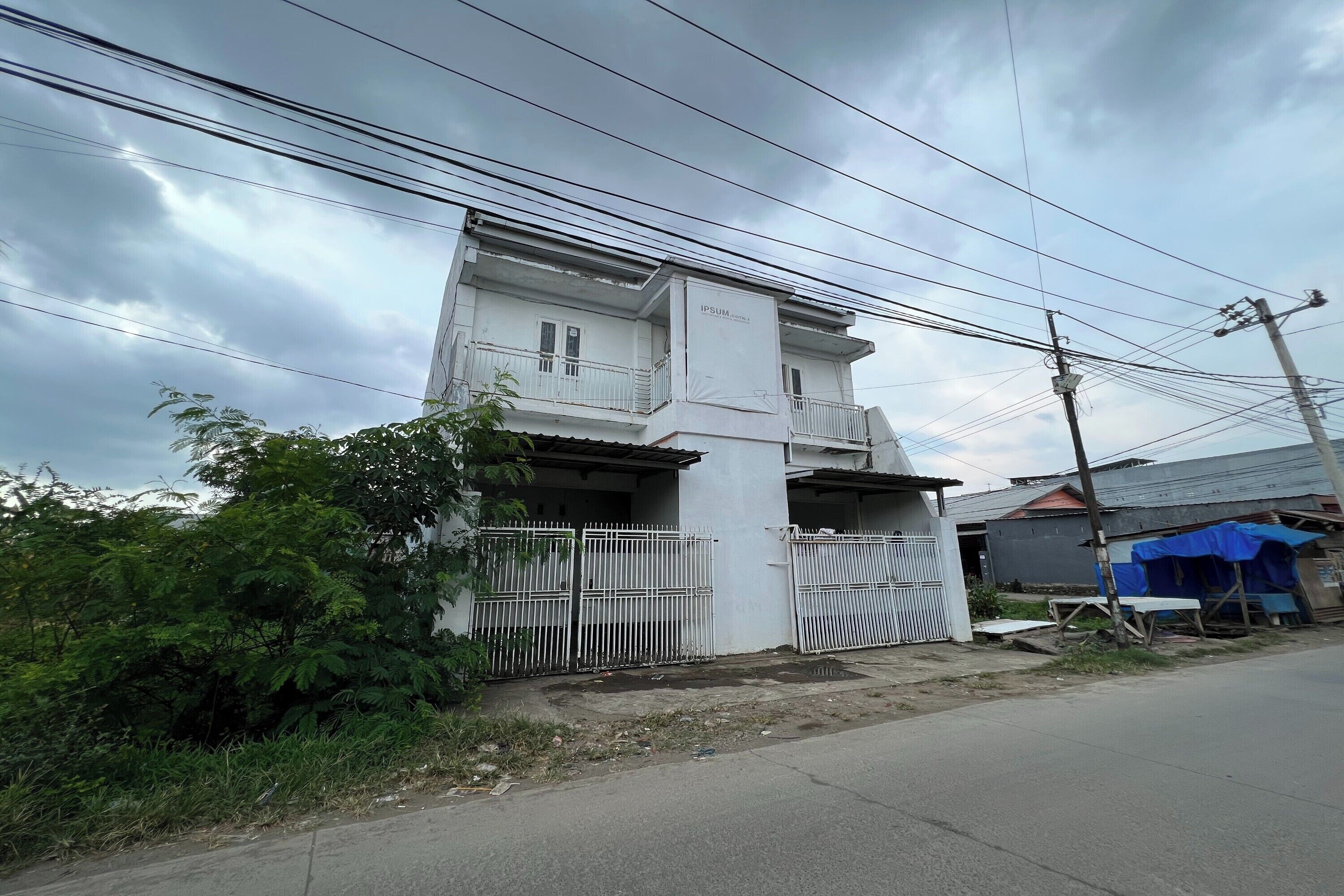 Un edificio de dos plantas con fachada blanca y entrada protegida por una reja.