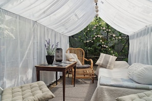 Una habitación con carpa, una silla de mimbre, una mesa con un florero y una cama con almohadas.