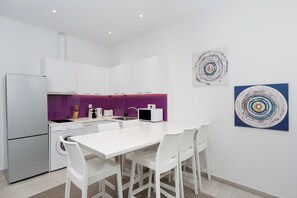 A modern kitchen with white cabinets, a purple backsplash, and a dining area with white chairs. - Spacious Modern Apt in Athens near Metro (Athens)