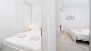 Ein modernes Hotelzimmer mit einem großen Bett, einem kleineren Bett und einem Fenster mit durchsichtigen Vorhängen.