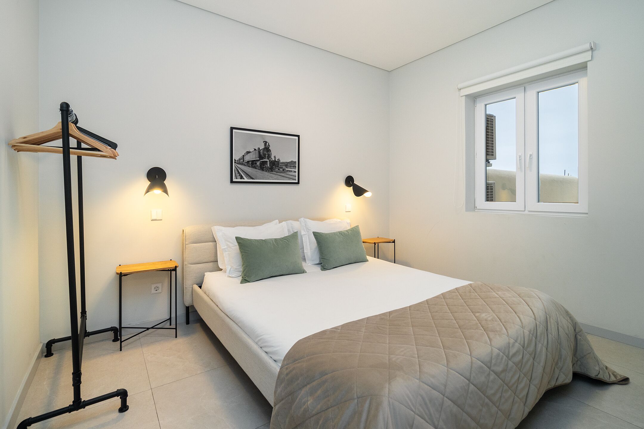 Una camera da letto con un letto, due comodini, una lampada a sospensione, un quadro al muro e una finestra.
