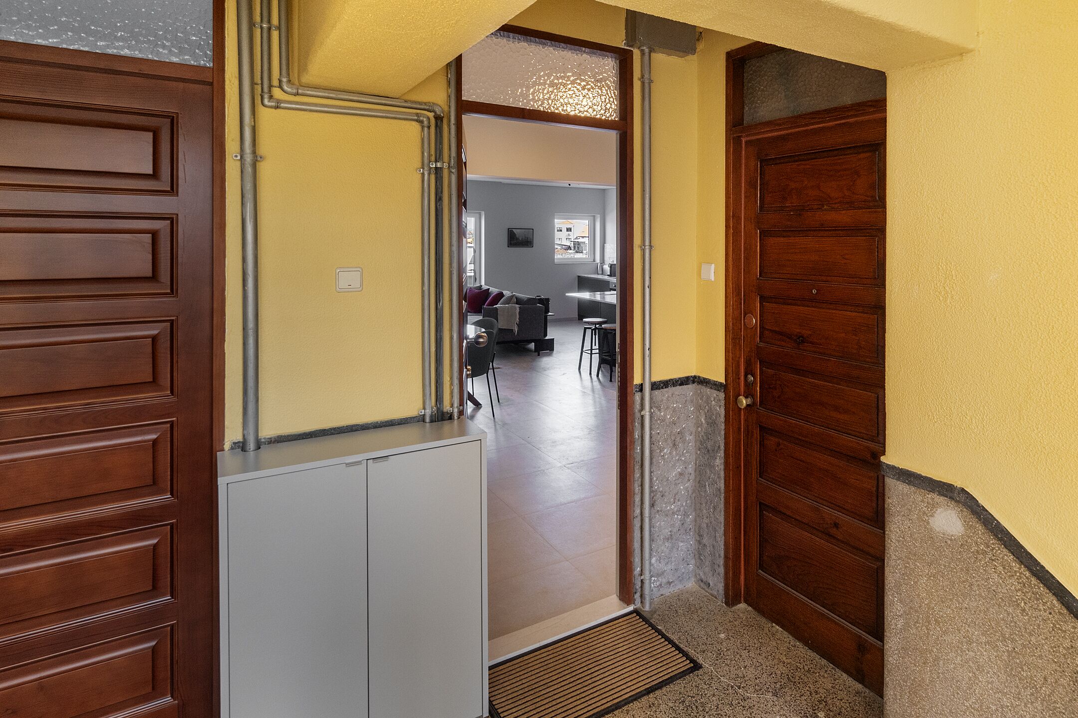A hallway leading to a living area with a kitchen in the background.