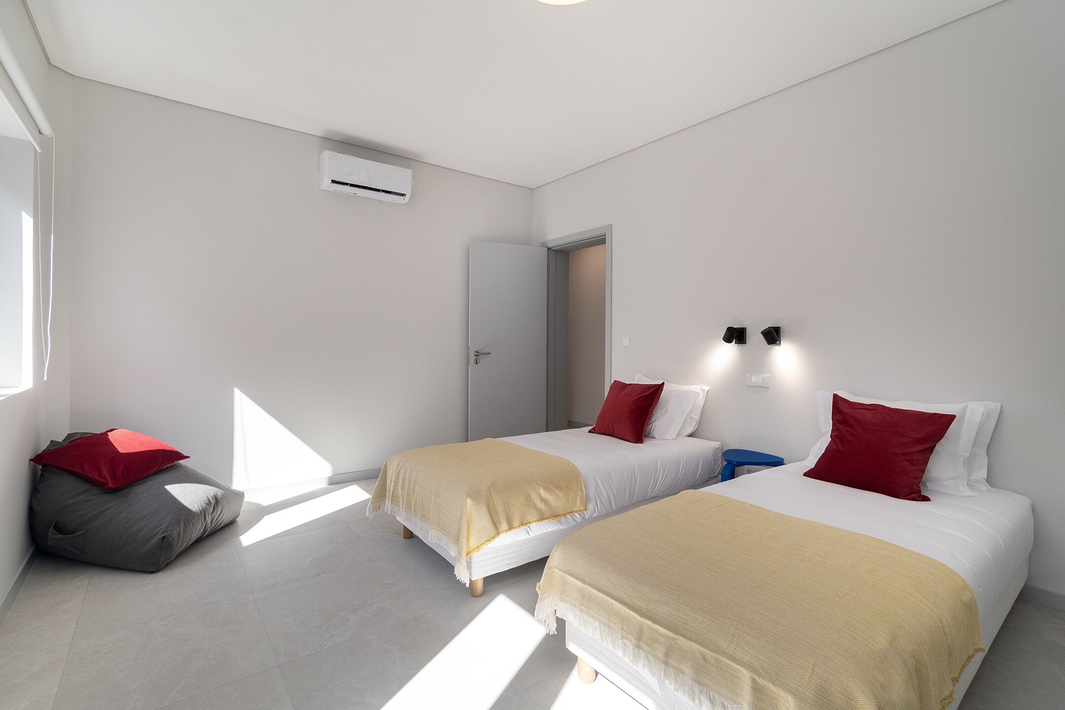 A modern hotel room with two beds, a bean bag chair, and a small desk.