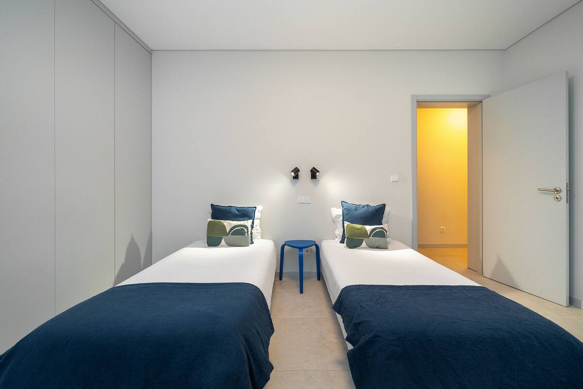A room with two single beds, a small table, and a door leading to another room.