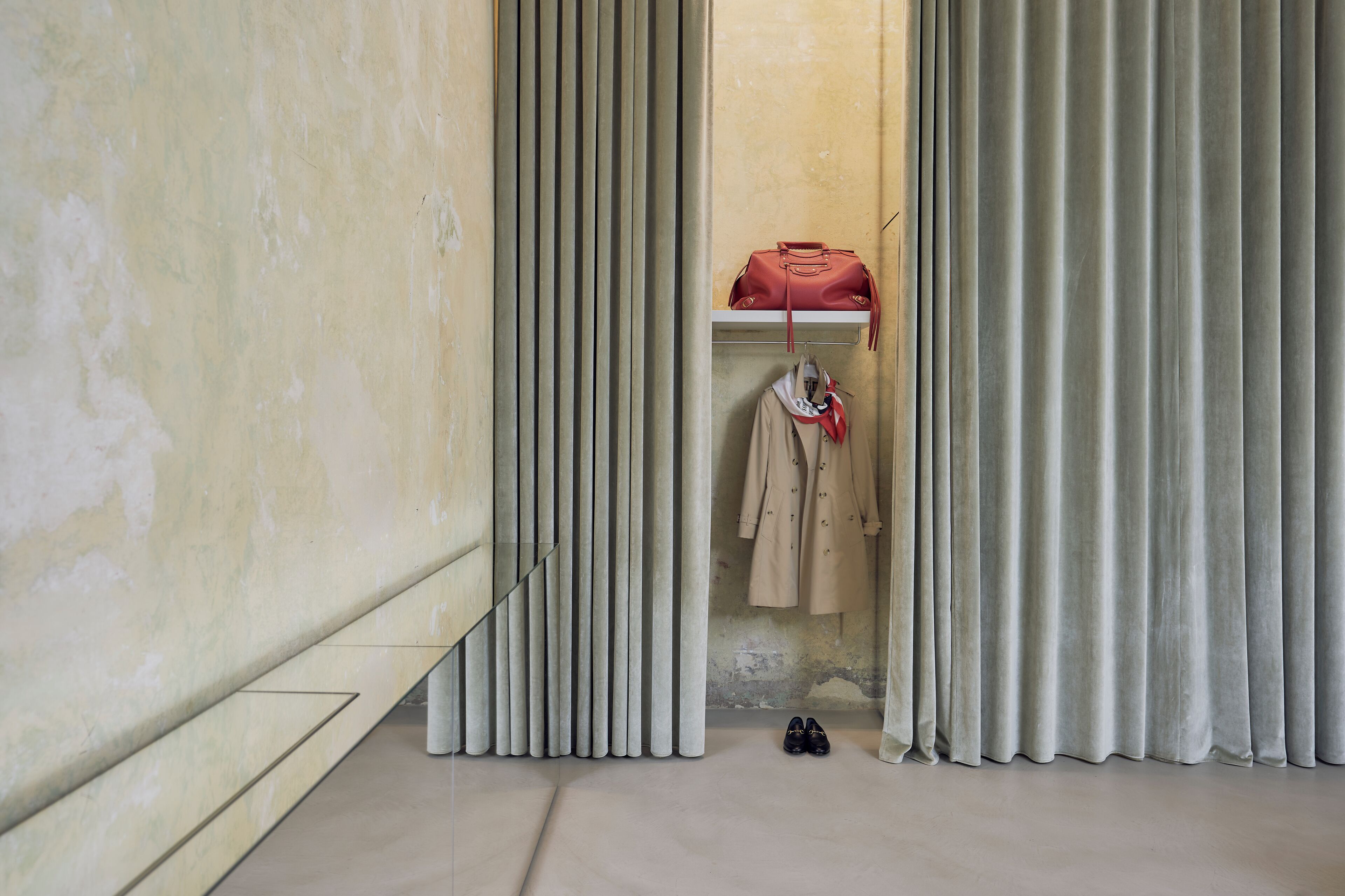 A room with a closet containing a red bag, beige coat, and black shoes.