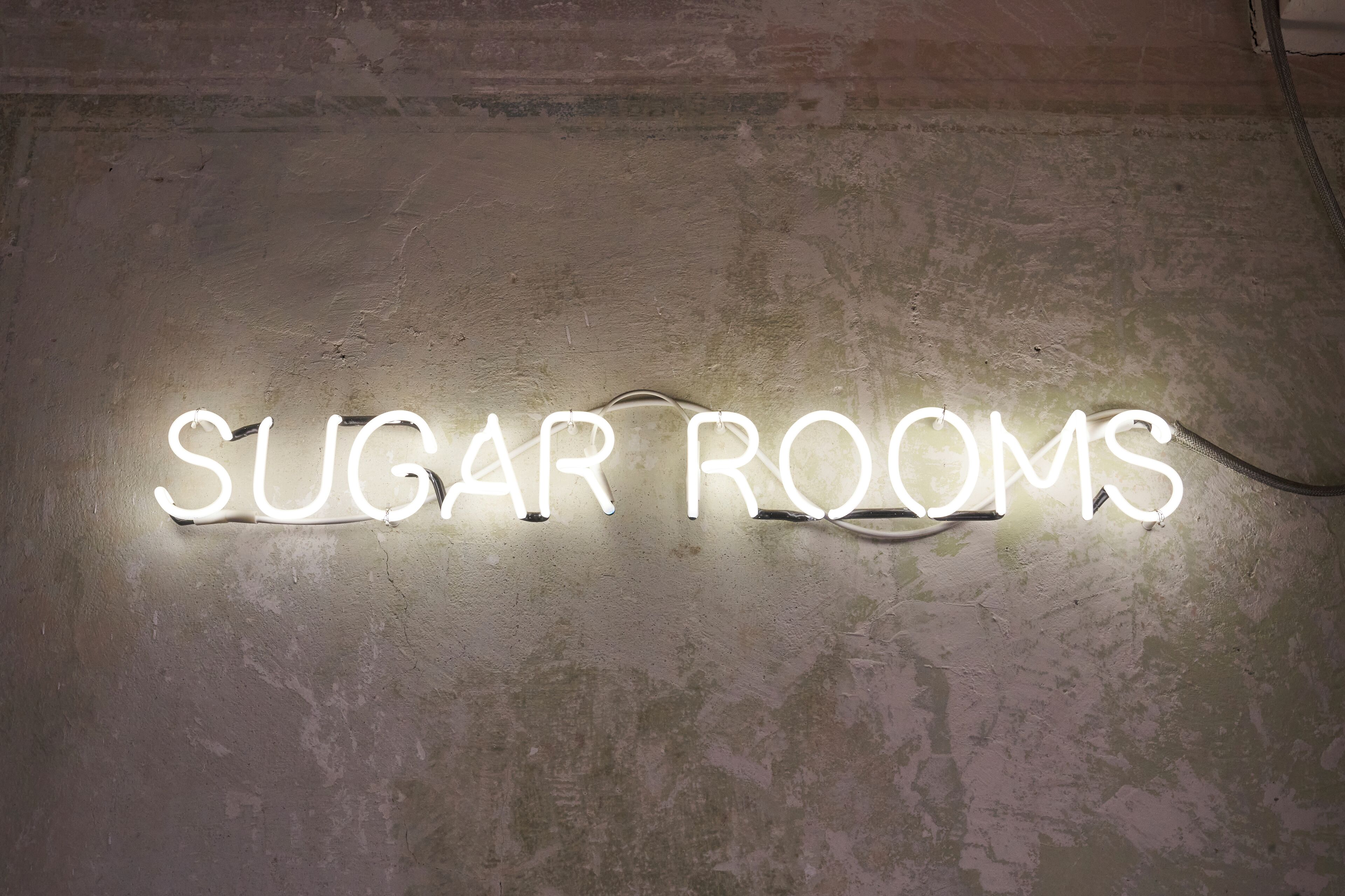A neon sign on a textured wall that reads "SUGAR ROOMS."