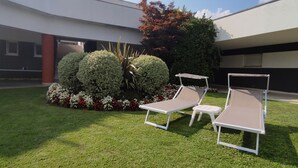 A modern outdoor area with two lounge chairs, a small table, and a well-maintained lawn with flower beds. - Il Parco (Montorfano)