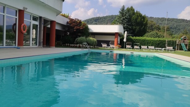 A swimming pool with a clear view of the surrounding area, including a building with large windows and a lifebuoy hanging on the wall. - Il Parco (Montorfano)