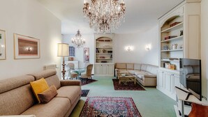A living room with a beige sofa, a coffee table, a TV, a bookshelf, and a chandelier. - Il Parco (Montorfano)