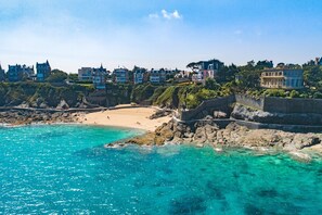 A coastal town with a sandy beach, clear turquoise waters, and a stone wall.