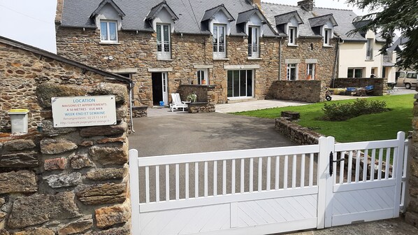 A stone building with a white gate, a sign indicating it is a location for maisonettes and apartments, and a paved driveway leading to the entrance.