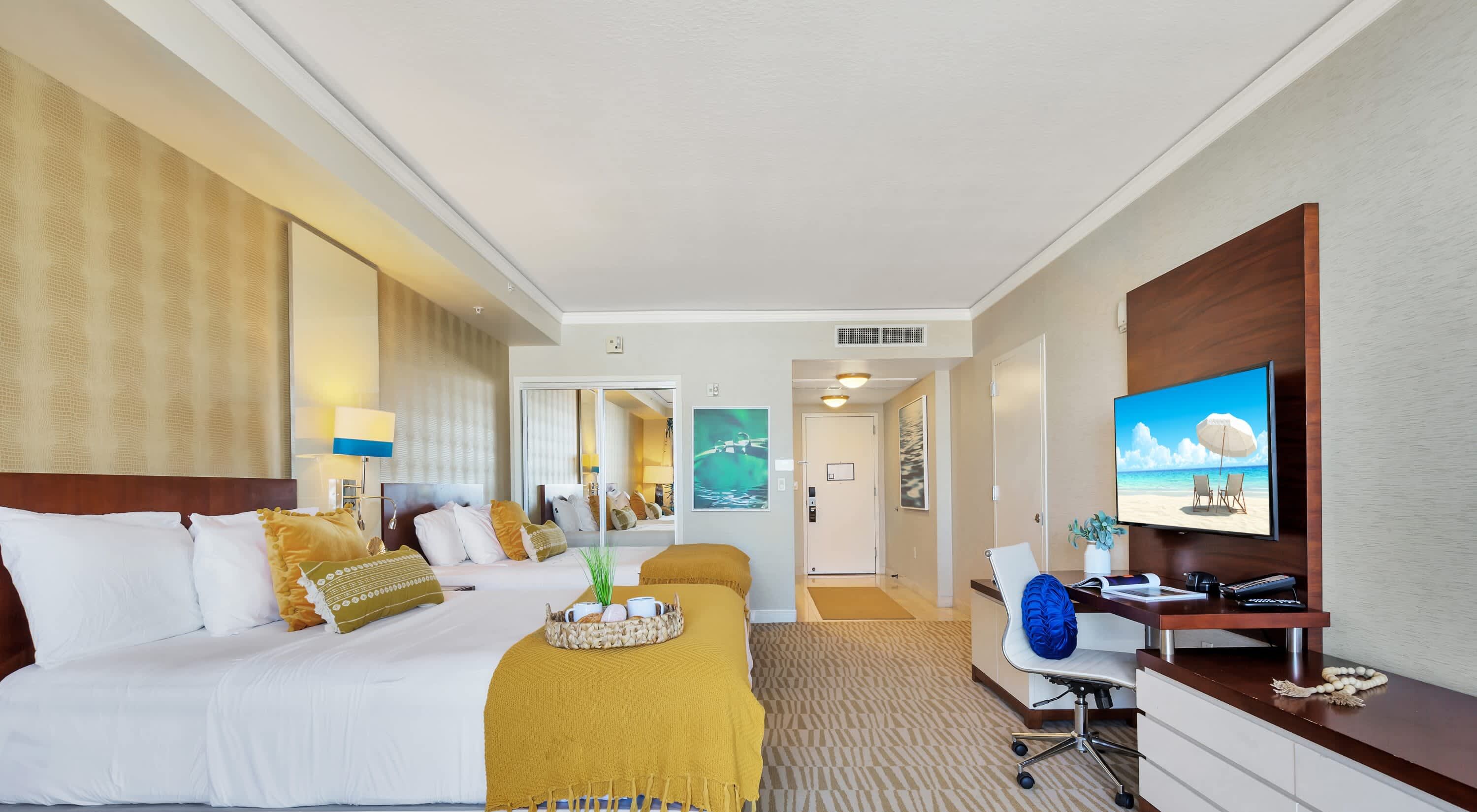 Une chambre d’hôtel avec un lit, un bureau, une télévision et une vue sur la plage.