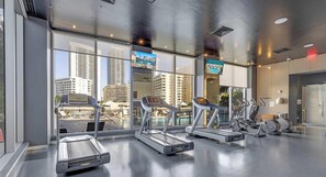 Un gimnasio con cintas de correr y bicicletas estáticas, amplias ventanas con vistas a la ciudad y un diseño moderno.