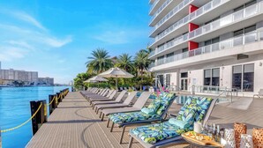 A poolside area with lounge chairs, umbrellas, and a view of the water. - Spectacular Apartment, Balcony View, Amazing Pool (Hallandale Beach)