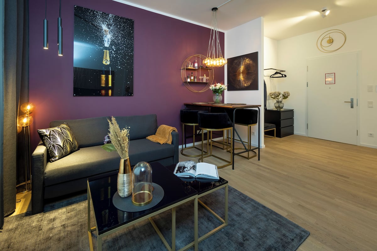 A modern living room with a dark sofa, a glass coffee table, and a dining area with a black chair and a small table.