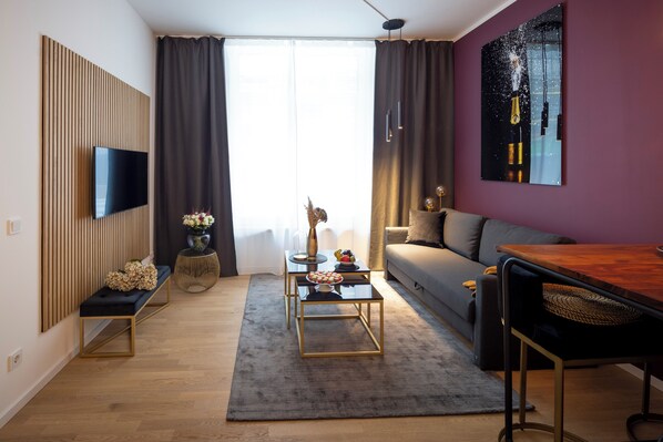 A modern living room with a flat-screen TV mounted on a wooden panel, a sofa, a coffee table, and a dining table.