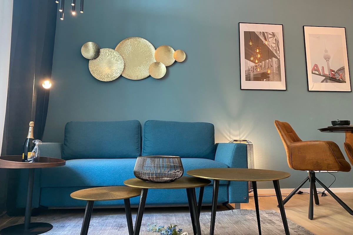 A modern living room with a blue sofa, two small round tables, a decorative wall piece, and framed pictures.