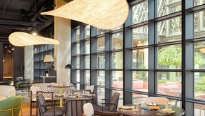 A modern interior with large windows, multiple seating areas, and hanging pendant lights. - Pullman Zagreb (Zagreb)