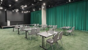 A conference room with green carpet, grey chairs, and tables, a stage with a screen, and a green curtain backdrop. - Pullman Zagreb (Zagreb)