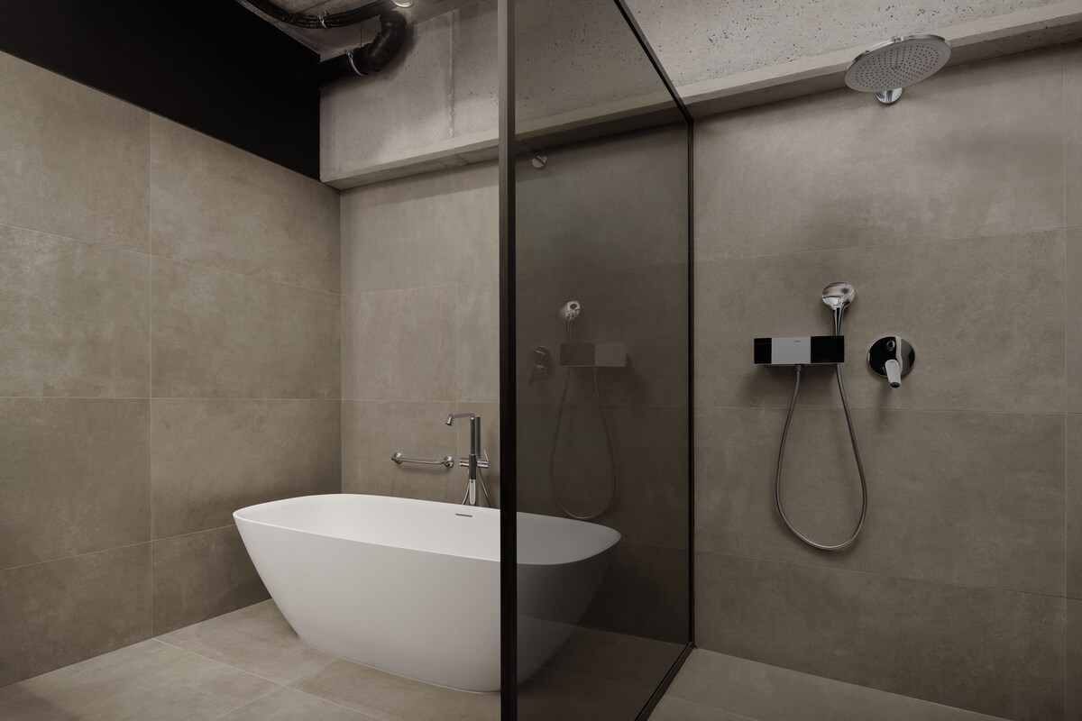 A modern bathroom with a freestanding bathtub, a glass-enclosed shower area, and a wall-mounted control panel.