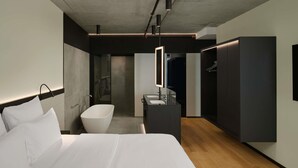 A modern hotel room with a large bed, a bathtub, a vanity with a mirror, and a walk-in closet. - Pullman Zagreb (Zagreb)