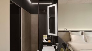 A modern hotel room with a large mirror, a bed, a bedside table with toiletries, and a nightstand with decorative items. - Pullman Zagreb (Zagreb)