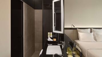 A modern hotel room with a large mirror, a bed, a bedside table with toiletries, and a nightstand with decorative items.