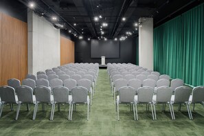 A conference room with rows of grey chairs, a stage with a projector, and a green curtain backdrop. - Pullman Zagreb (Zagreb)