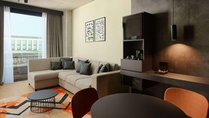 A modern living room with a sectional sofa, a coffee table, and a dining area with chairs. There are abstract wall art pieces and a built-in shelving unit. - Pullman Zagreb (Zagreb)