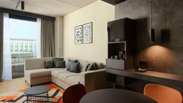 A modern living room with a sectional sofa, a coffee table, and a dining area with chairs. There are abstract wall art pieces and a built-in shelving unit.