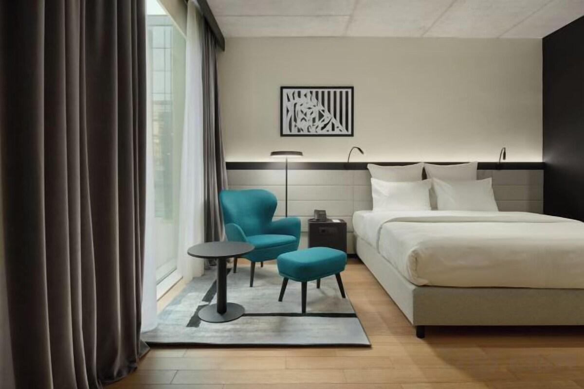 A modern hotel room with a bed, a desk, a chair, and a floor lamp.