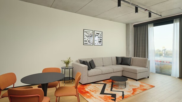 A modern living room with a grey sectional sofa, orange chairs, a round table, and a large window with curtains. - Pullman Zagreb (Zagreb)