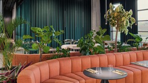 A modern indoor seating area with orange cushioned sofas, round tables, and potted plants. - Pullman Zagreb (Zagreb)