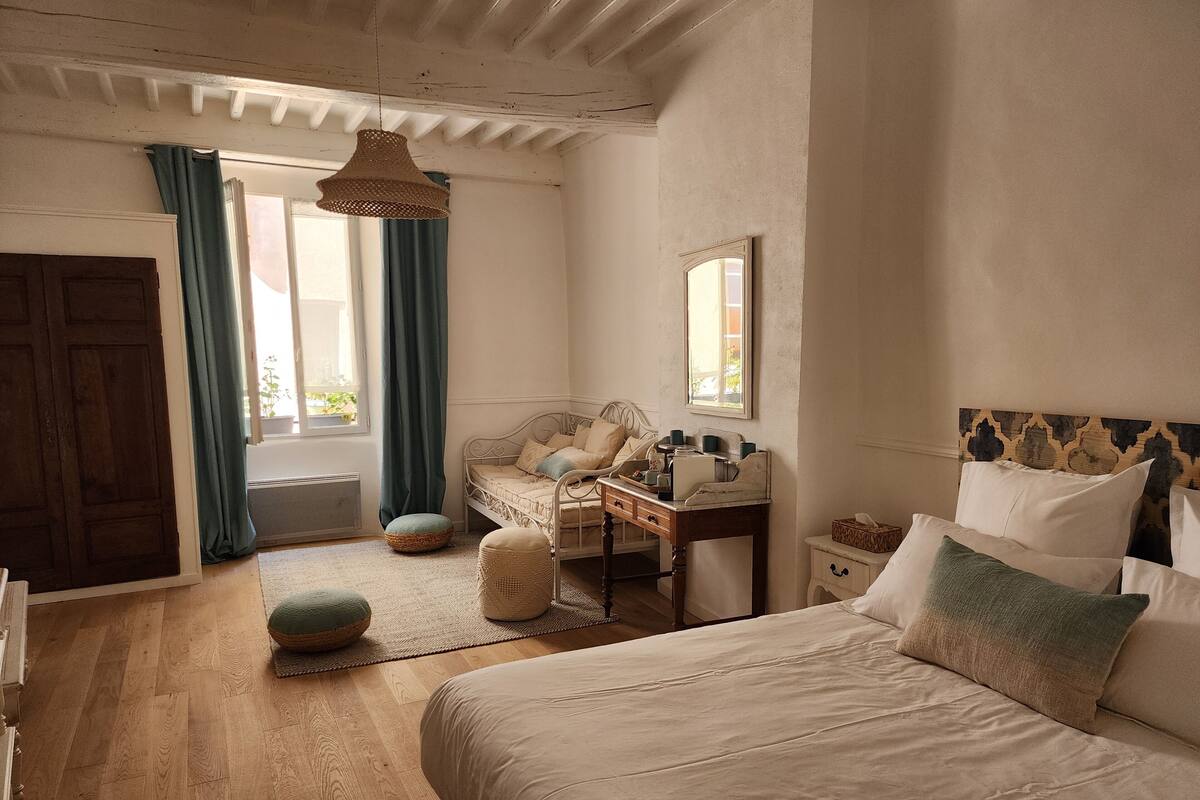 A bedroom with a bed, a dresser, a vanity, and a window with curtains.