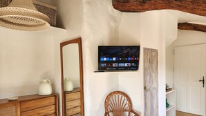 Una habitación con un aparador de madera, una silla de mimbre, un televisor montado en la pared y una puerta blanca.