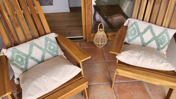 Two wooden chairs with cushions, a woven lantern, and a view of a room with a window and a potted plant.