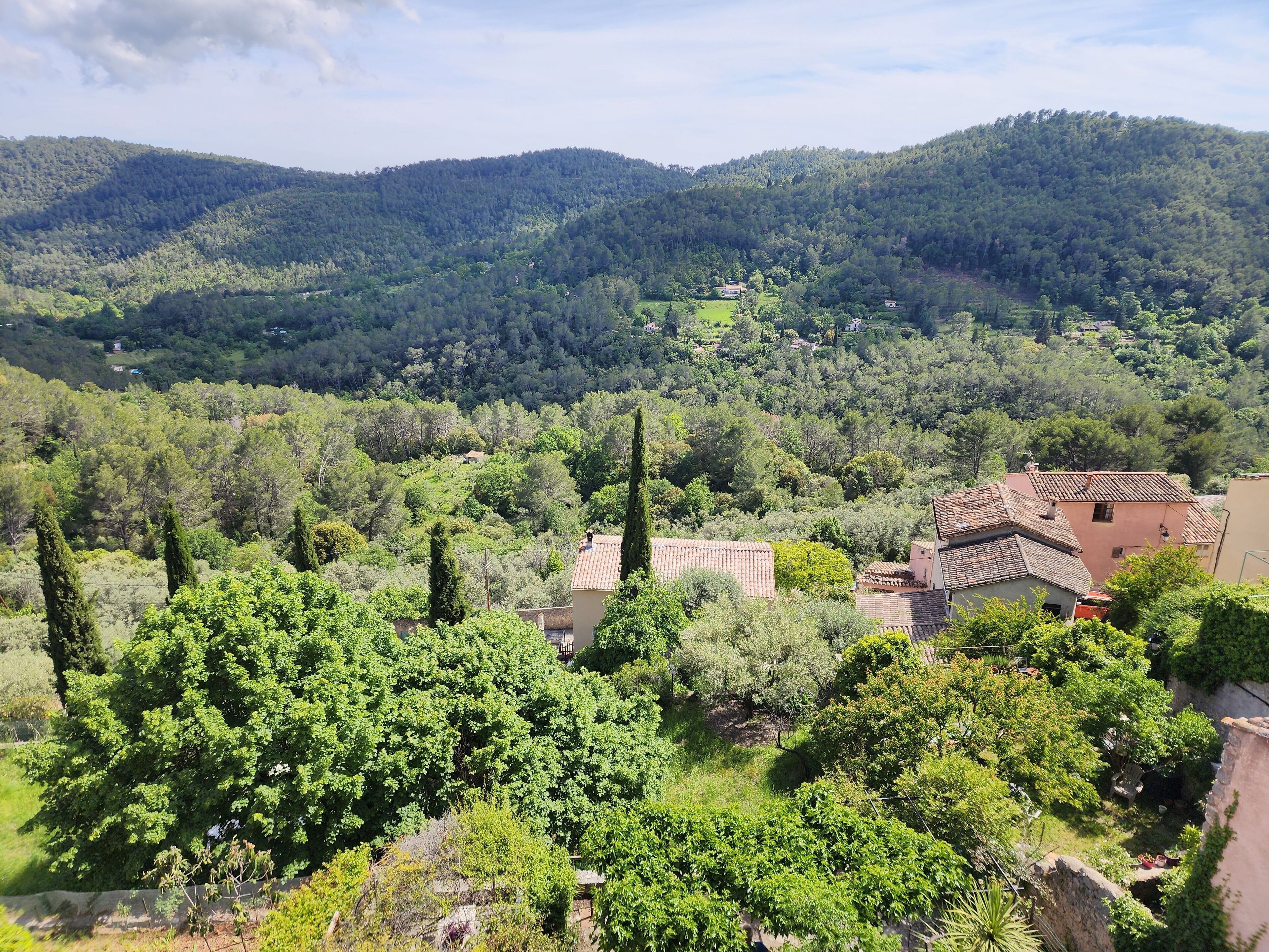 Un paysage rural avec une maison entourée d’une végétation luxuriante et des collines en arrière-plan.
