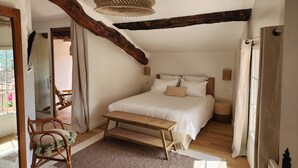 Un dormitorio con una cama grande, un banco de madera, una lámpara de fibra tejida y vigas de madera a la vista.
