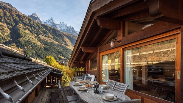 Une terrasse en bois avec une table dressée pour le repas, offrant une vue sur un paysage montagneux.