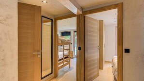 Un couloir avec des portes en bois menant à une chambre où se trouve un lit superposé.