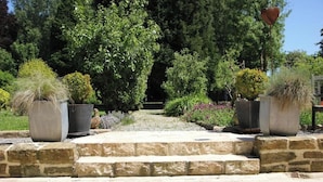 A garden pathway with stone steps leading to a lush green area with various plants and trees.